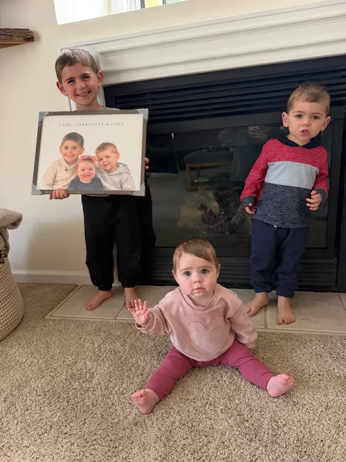 Three siblings holding their custom illustrated portrait above the fireplace