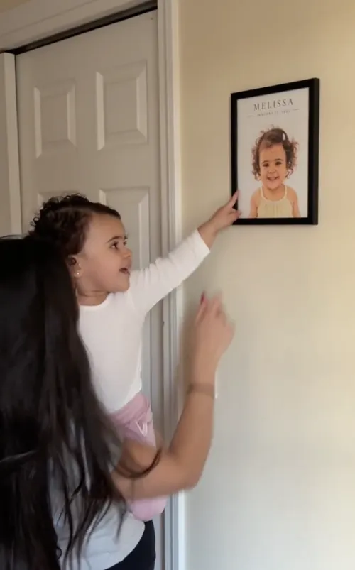 Toddler excitedly pointing at her own framed portrait on the wall