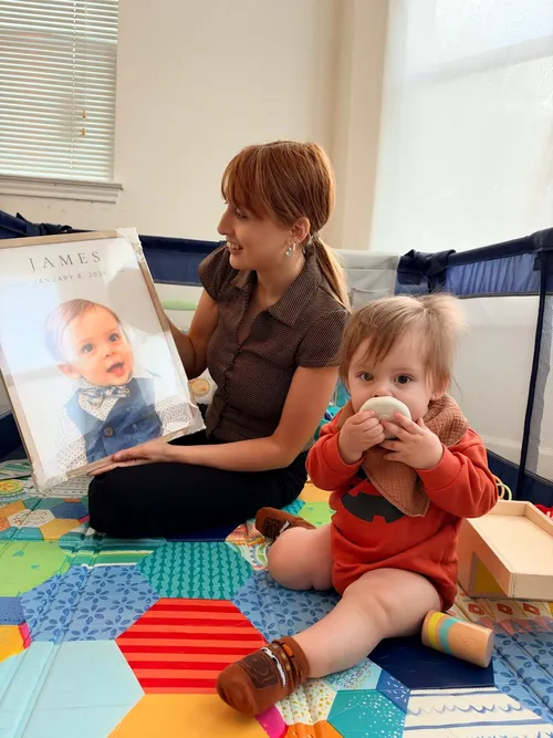 A mom holding baby James's framed portrait beside him on a play mat