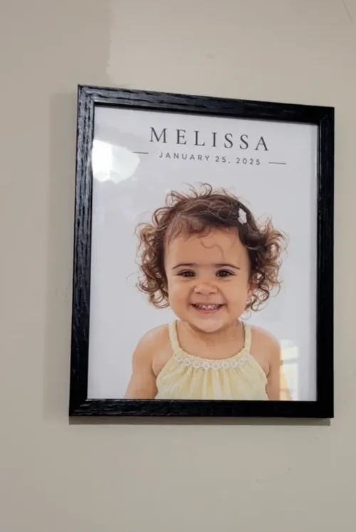 A black framed baby portrait hanging on a wall